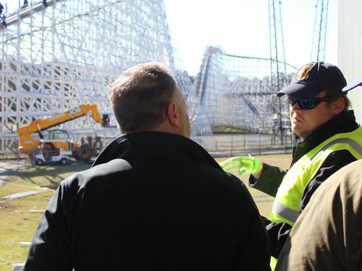 Engineers talking with a roller coaster under construction in the background.