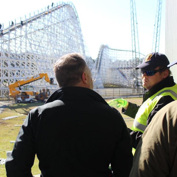 Engineers talking with a roller coaster under construction in the background.